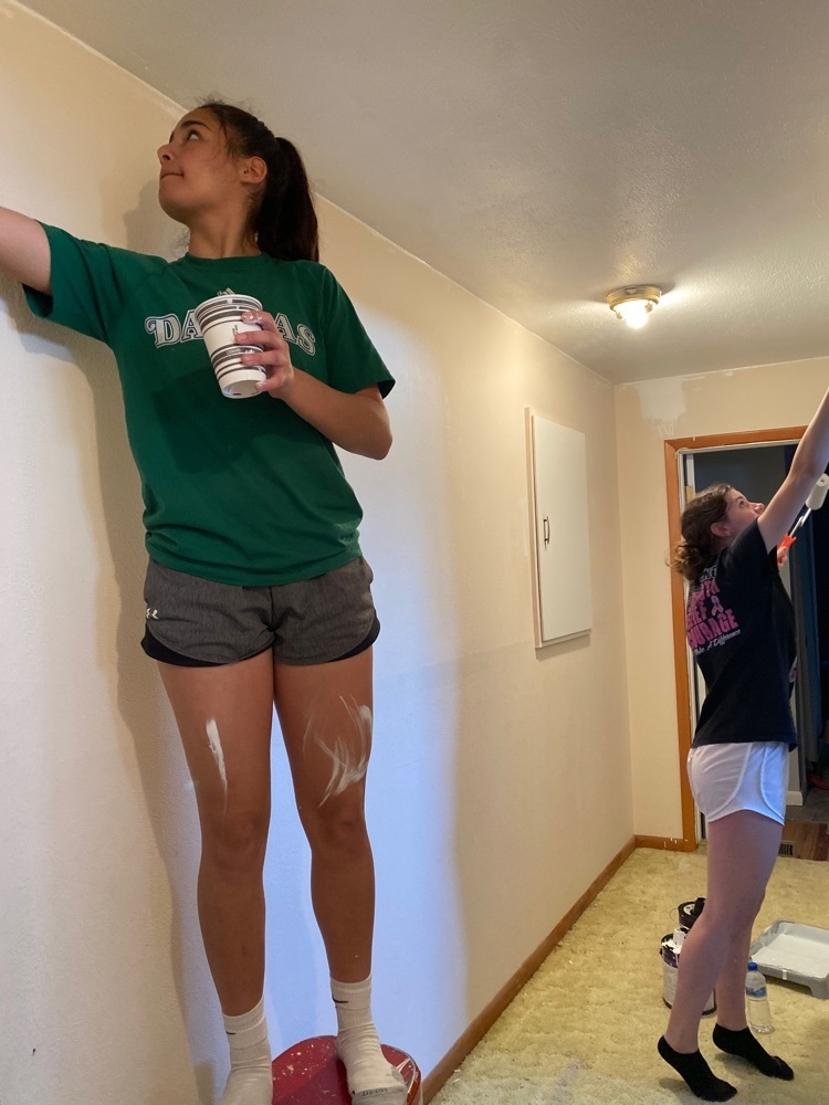Two girls in painting clothes are seen candidly painting a hallway wall 